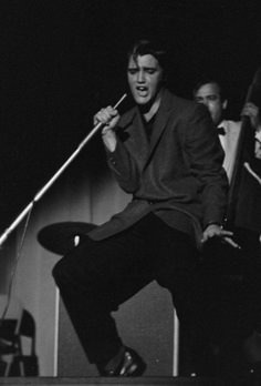 the man is singing on stage with two microphones in his hand and another person standing behind him