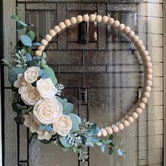 a wreath with white flowers and greenery hanging on the front door to welcome guests