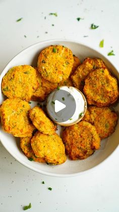 a white bowl filled with crab cakes next to a small bottle of ranch dressing on the side