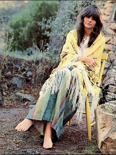 a woman sitting in a chair next to a rock and grass covered hillside with trees