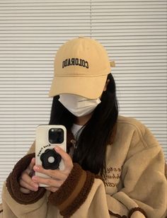 a woman wearing a hat and holding a camera taking a selfie in front of her face