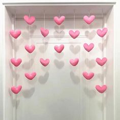 pink hearts hanging from the ceiling in front of a white wall with shadow on it