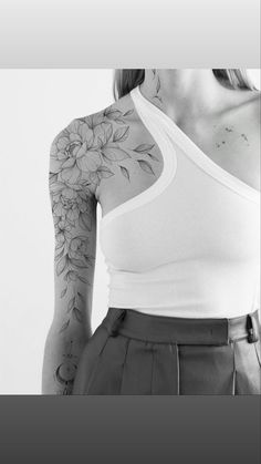 a woman with a flower tattoo on her left arm and shoulder, standing in front of a white wall