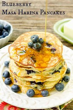 stack of pancakes with blueberries and syrup being drizzled on top