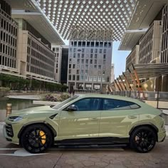 a light green suv parked in front of some tall buildings with black rims and yellow wheels