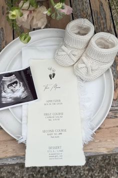 a white plate topped with baby booties next to a card and menu on top of a wooden table