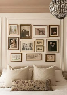 a white bed topped with lots of pillows and pictures on the wall next to a chandelier