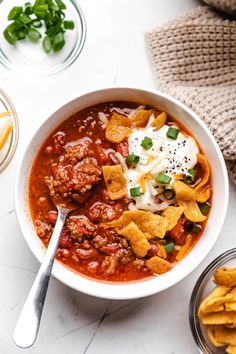 a bowl of chili with tortilla chips and sour cream on the side next to it