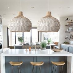 two pendant lights hanging from the ceiling above a kitchen island with stools in front of it