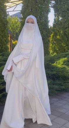 a woman in a white dress and veil walking down the street with her hands on her hips