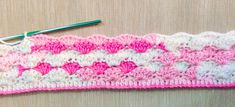 a crocheted pink and white piece of cloth with a green hook on it