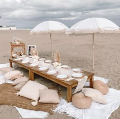 a picnic table set up on the beach with plates and napkins under umbrellas