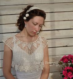 a woman in a white dress cutting a cake on a table with flowers behind her