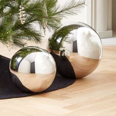 two shiny metal balls sitting on top of a wooden floor next to a pine tree