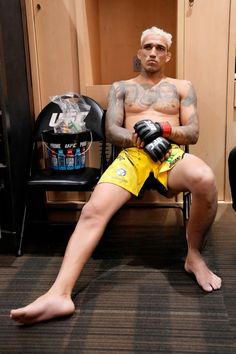 a man sitting in a chair with his legs crossed and tattoos on the chest, wearing boxing gloves