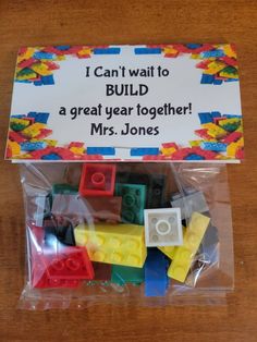 a plastic bag filled with lots of legos on top of a wooden table next to a sign that says, i can't wait to build a great year together mrs jones