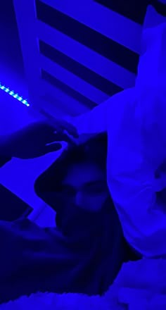 a person laying on a bed in a room with blue light coming from the ceiling