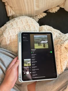 someone is holding an ipad in their lap while sitting on a couch with a blanket