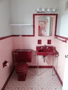 a bathroom with pink and red tiles on the walls, toilet, sink and mirror