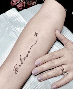 a woman's arm with a tattoo on it that says believe and an arrow