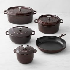 four cast iron pots and pans on a white countertop, with the lids off