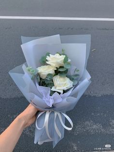 a person holding a bouquet of white roses on the side of the road with their hand