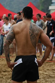 a man standing on top of a sandy beach next to a group of people wearing swim trunks