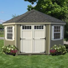 a small shed with two windows on the roof and flowers in the grass around it