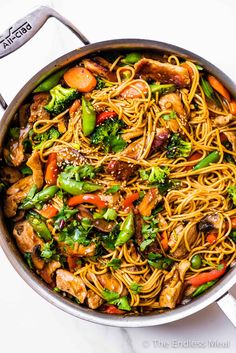 a pan filled with noodles and vegetables on top of a white countertop next to utensils