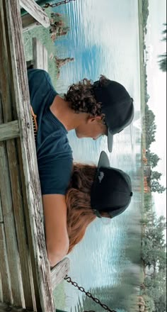 two people wearing hats standing next to each other in front of a body of water