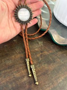 This awesome bolo tie has a southwestern brass sun design and pearl white stone centerpiece.  The cord is brown genuine leather. Our bolos pair nicely with many of our belt buckles! They make wonderful gifts.    The western bolo tie rope length is 39'' ; charm pendant size is 1 1/2'' Adjustable Gold Western Bolo Ties, Vintage Bolo Ties With Adjustable Length For Western-themed Events, Vintage Bolo Ties With Adjustable Length For Rodeo, Bohemian Bolo Ties For Western-themed Events, Vintage Bolo Tie With Adjustable Length For Western Events, Hand Tooled Brown Jewelry For Rodeo, Brown Hand Tooled Jewelry For Rodeo, Vintage Lariat Bolo Ties For Ranch, Vintage Lariat Bolo Tie For Ranch