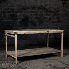 a wooden table sitting on top of a floor next to a brick wall in an empty room