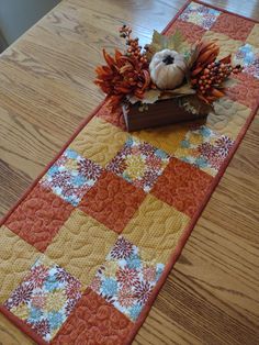 a quilted table runner with a teddy bear sitting on top of it and flowers in the center