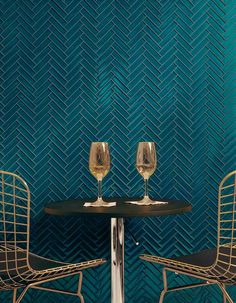 two wine glasses sitting on top of a table next to each other in front of a blue wall