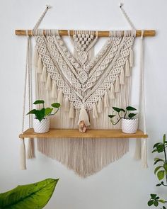 a macrame wall hanging with potted plants in front of it on a wooden shelf