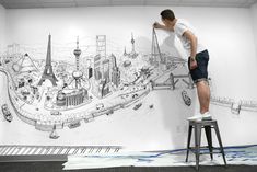 a man standing on top of a stool in front of a wall painting with a cityscape