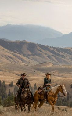 two people are riding horses in the field with mountains in the backgrouds