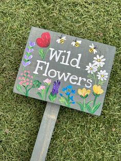 a sign that is on the grass with flowers painted on it, says wild flowers