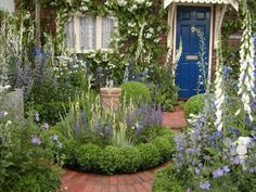 a blue door surrounded by flowers and greenery in front of a brick building with white trim