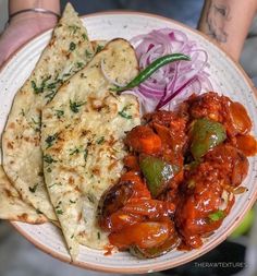 a person holding a plate with food on it and some onions, carrots, and pita bread