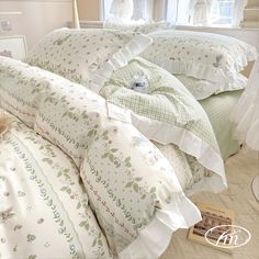 a bed with white and green comforters in a bedroom next to a book on the floor