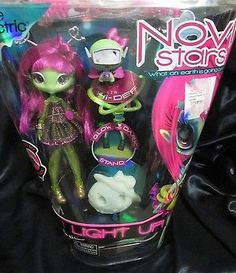 a box with two dolls in it sitting on a black cloth covered surface, one has pink hair and the other has green eyes