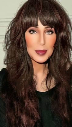 a woman with long brown hair and bangs wearing a black top is posing for the camera