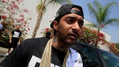 a man in a black shirt and hat with chains around his neck standing next to a car