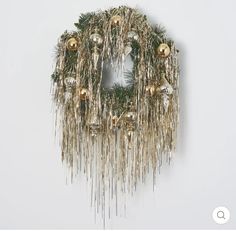 a christmas wreath hanging from the side of a white wall with gold ornaments on it