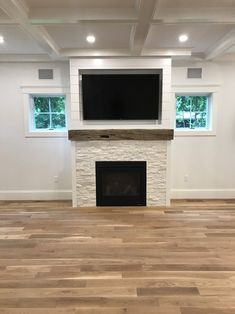 an empty living room with wood floors and a flat screen tv on the fireplace mantel