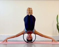 a woman doing a handstand on top of a pink mat in front of a white wall