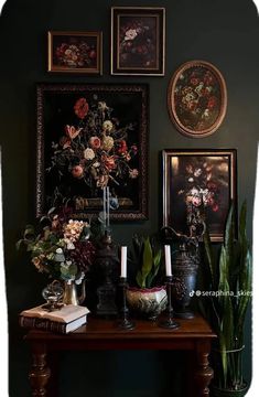 a table with flowers and candles on it in front of some framed pictures above it