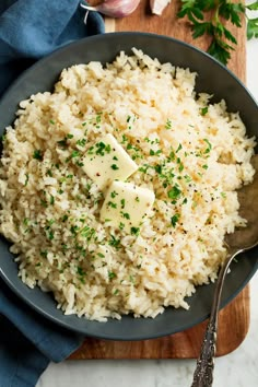 a bowl filled with rice and parsley on top of a wooden cutting board next to garlic