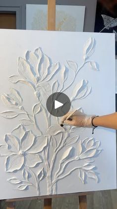 a person is working on an art piece with white paint and flowers in the background